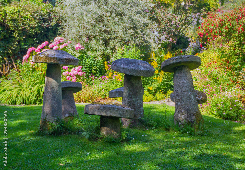 Seven stone staddle stones, ornamental toadstools, in dappled sunlight. Old, weathered fairy stones covered with lichen and moss in summer garden. Seven stone staddle stones, ornamental toadstools, in dappled sunlight. Old, weathered fairy stones covered with lichen and moss in summer garden.