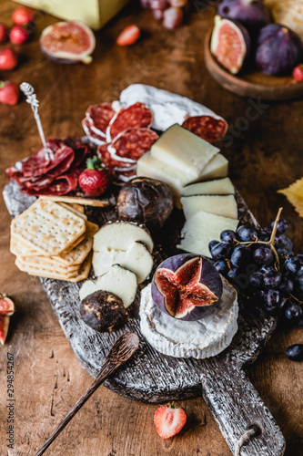 assortment of cheese on wooden board with fruits, honey and ham on brown wooden table, selective focus
