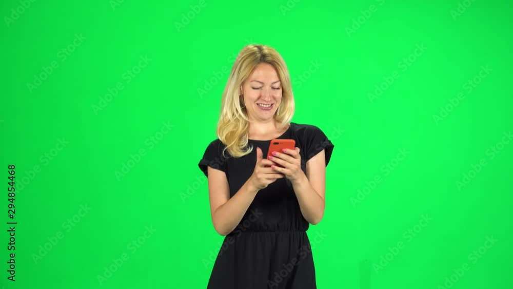 Smiling woman goes and texting with smartphone on green screen at studio. Smiling woman goes and texting with smartphone on green screen at studio.