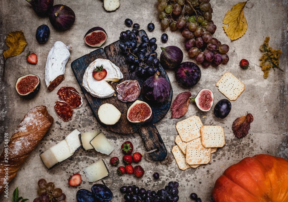 assortment of cheese with figs, grapes, ham and crackers on shabby background, top view