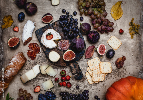 assortment of cheese with figs, grapes, ham and crackers on shabby background, top view