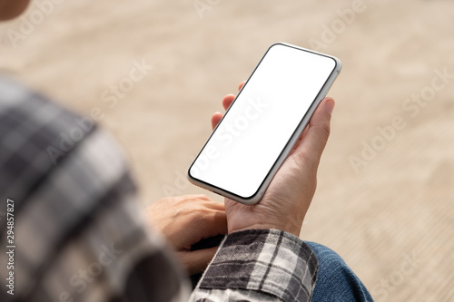Woman hand holding and using mobile phone with blank screen sitting in the outdoor