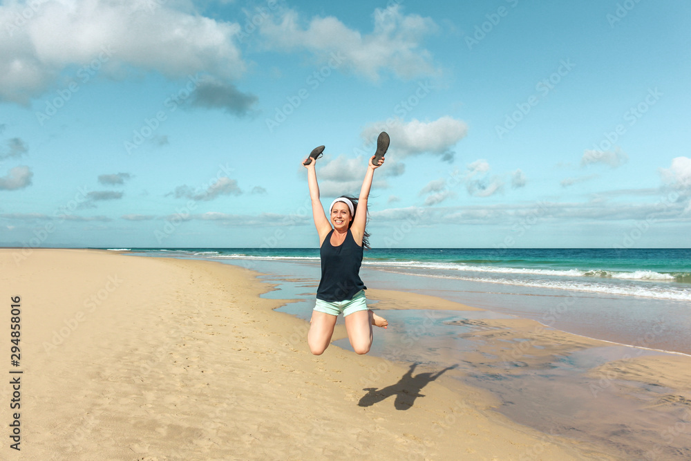 Young woman jumping smiling on the beach sand by the sea Young woman jumping smiling on the beach sand by the sea