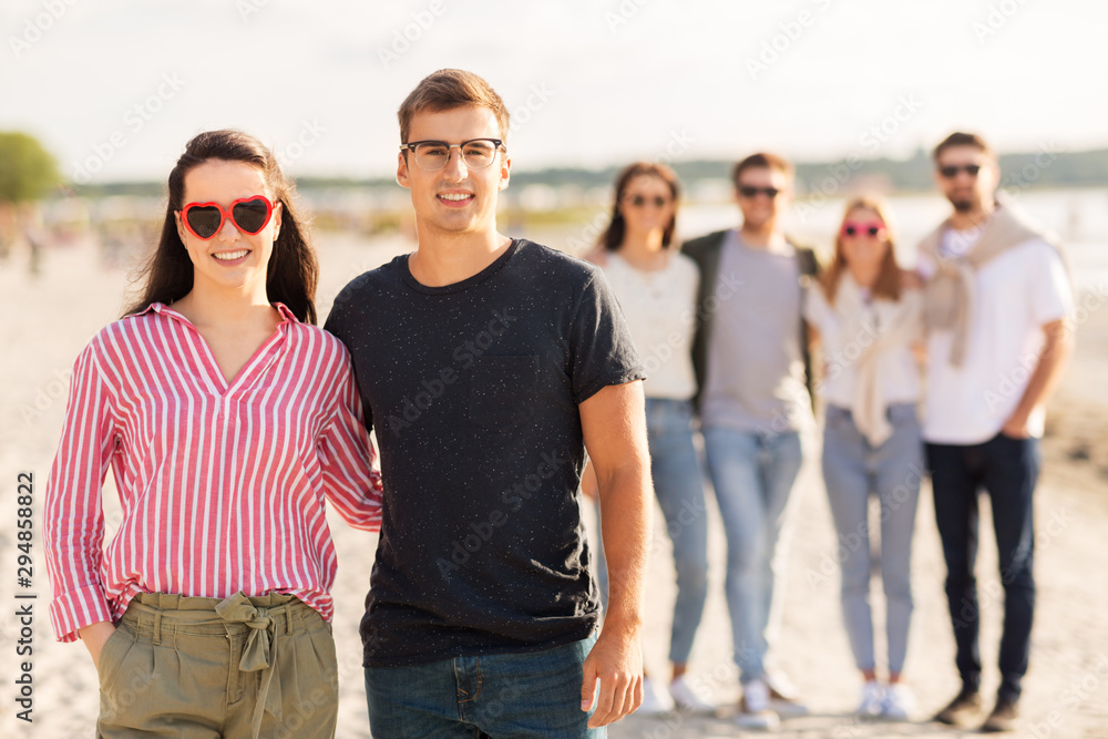 valentine's day, relationships and people concept - happy couple with group of friends on beach in summer