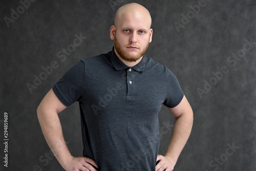 Portrait of a handsome bald man in a gray t-shirt on a gray background in the studio. Shows emotions in various poses.