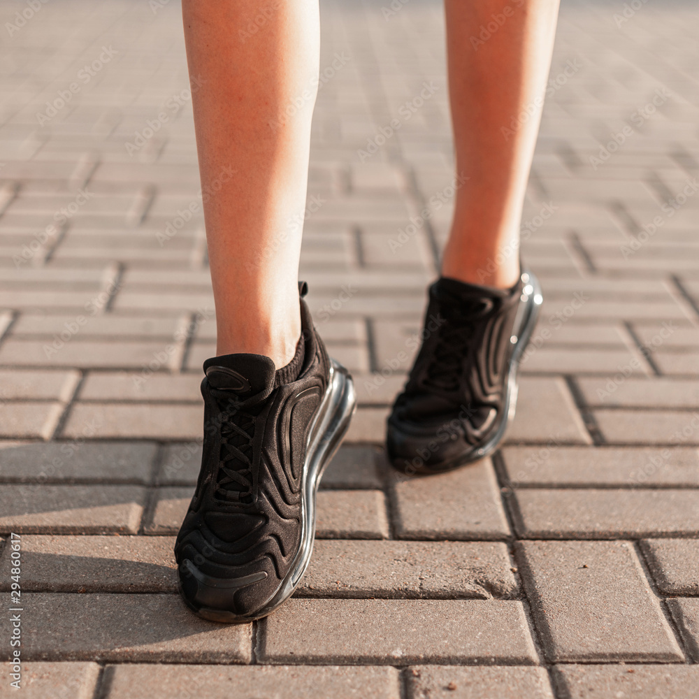 Modern young woman with slender beautiful legs in fashionable black sneakers  walks down the street. Stylish sporty women's shoes. Summer style. Closeup  of female legs with shoes. Stock Photo | Adobe Stock