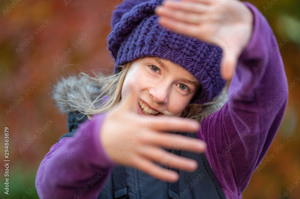 Smiling girl framing face with hands with blurry fall colors in the background Smiling girl framing face with hands with blurry fall colors in the background