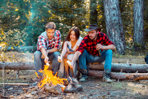 Friends relaxing near campfire after day hiking or gathering mushrooms. Friends enjoy weekend camp in forest. Enjoying camping holiday in countryside.
