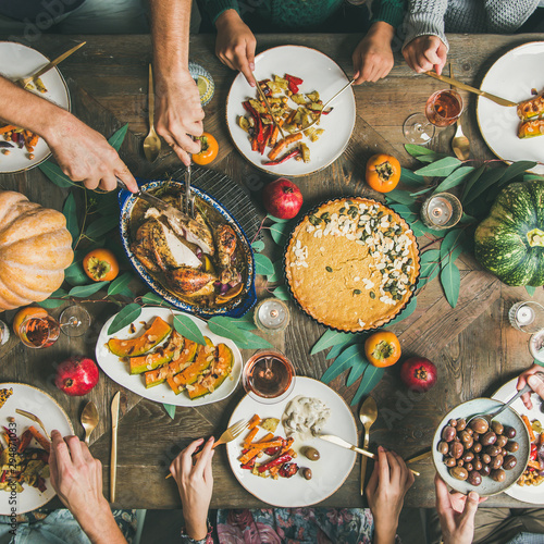 Thanksgiving or Friendsgiving holiday celebration party. Flat-lay of friends feasting at Thanksgiving Day table with turkey, pumpkin pie, roasted vegetables, fruit and rose wine, top view, square crop