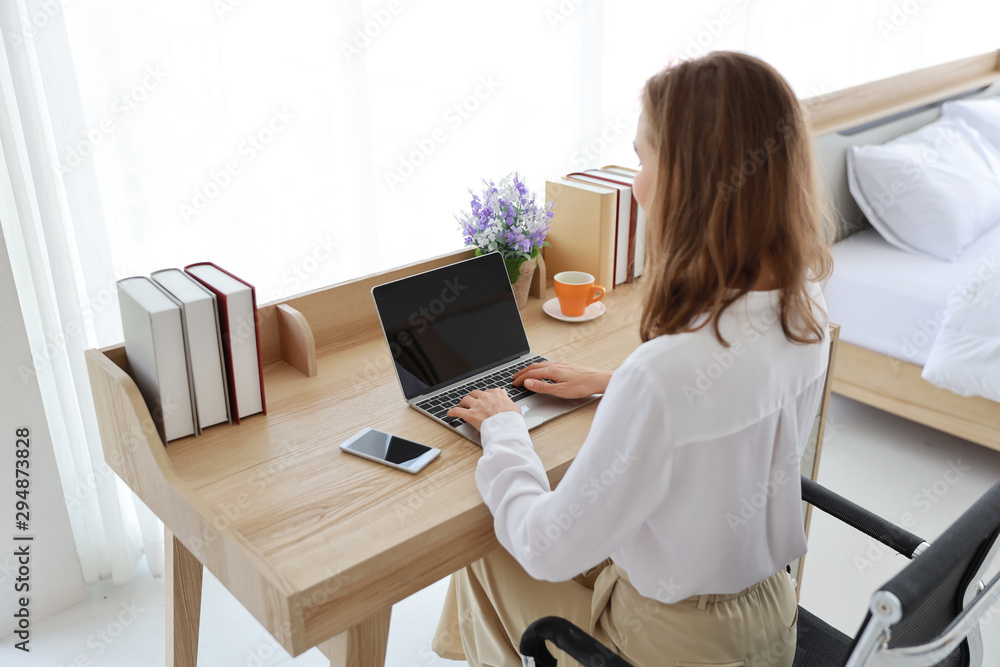 rear view beautiful caucasian girl drinking a cup of coffee or tea in the morning with laptop computer and cell phone on wood table in bedroom rear view beautiful caucasian girl drinking a cup of coffee or tea in the morning with laptop computer and cell phone on wood table in bedroom