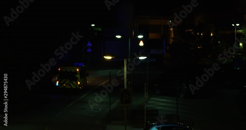  A British Ambulance With Flashing Blue Lights Leaving For An Emergency Late At Night. Driving to an Incident. Dark Dim Road With Passing Traffic.