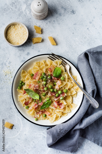 Fettuccine pasta with bacon and green peas and parmesan cheese in light plate on old gray concrete background. Top view.