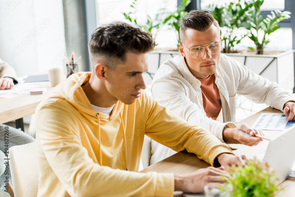 Fototapeta premium two young businessmen sitting at workplace and working together in office