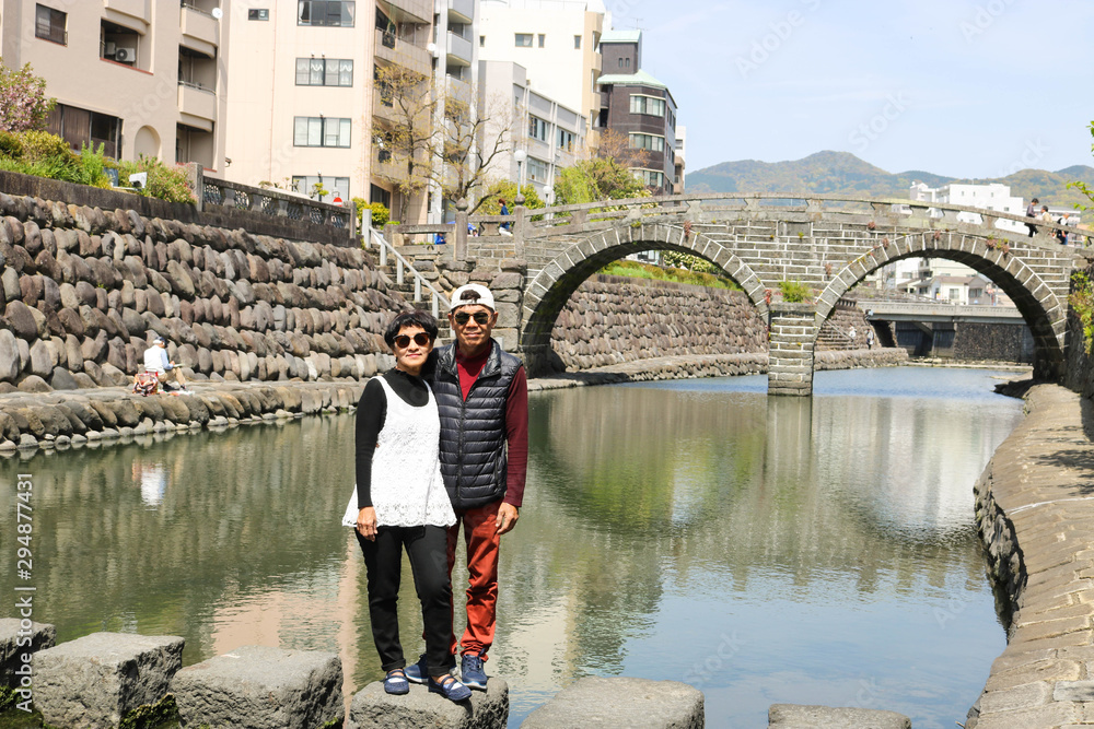 Senior couple posing at Meganebashi Bridge in Nagasaki, Japan. Meganebashi bridge is tourist attraction.