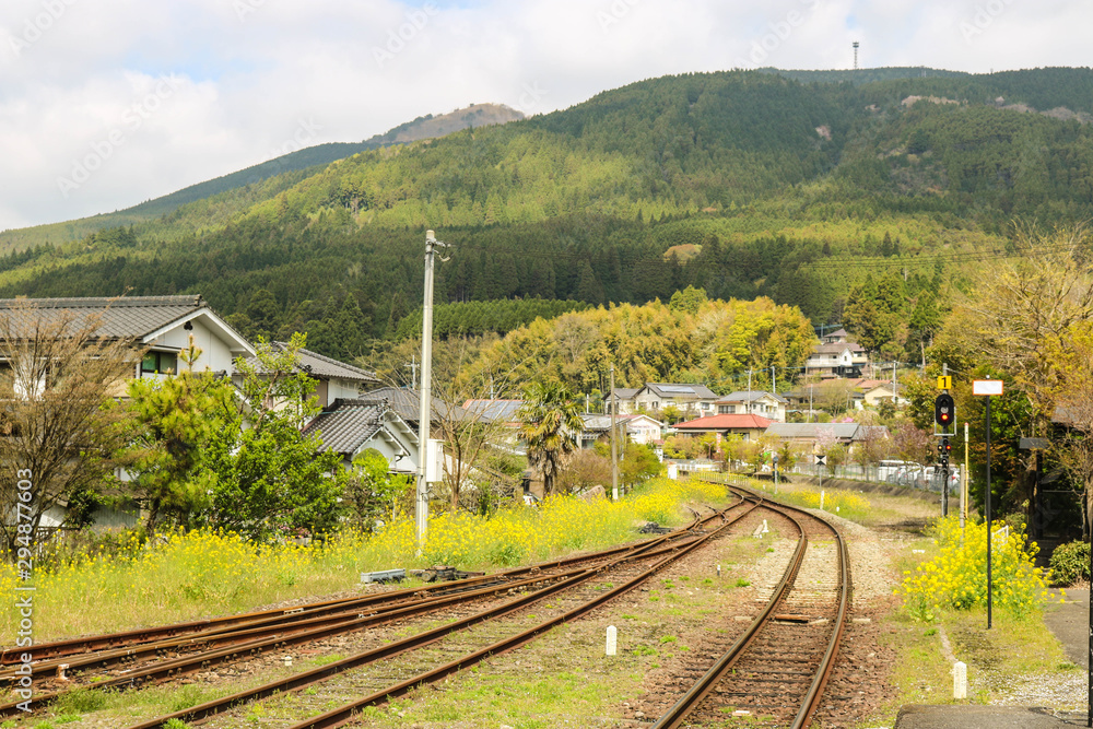 Fototapeta premium Railroad tracks through the village with nature and mountain background in spring season, Yufuin, Japan.