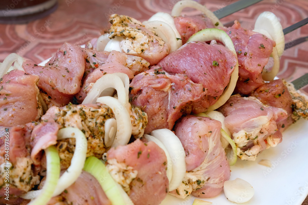 Raw pork meat with onions and spices for cooking kebabs on skewers on the grill. Marinated meat lies on a plate.