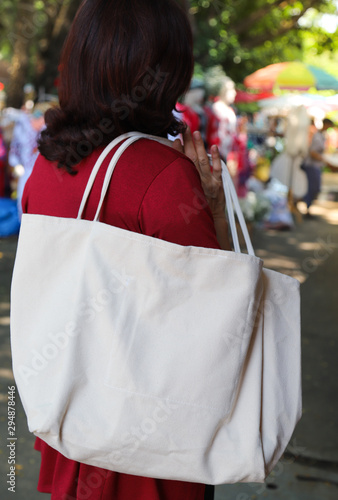 Closeup of white reusable cotton bag carrying by woman. Global friendly practice. Vertical view.