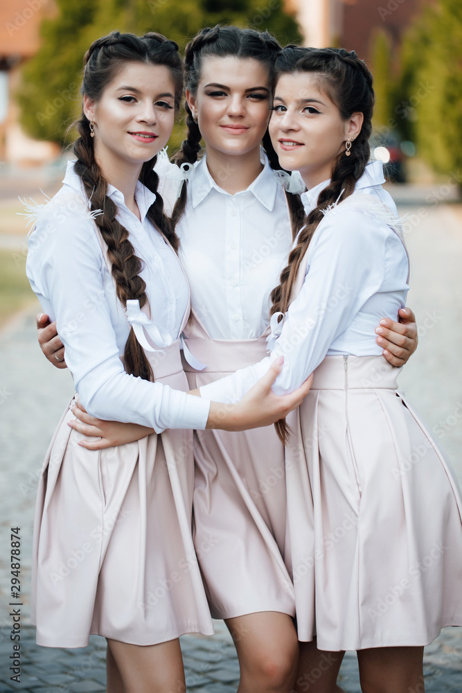 Two beautiful sisters twin girls in identical uniform, with makeup and hairdo with her friend. Concept of female friendship. Portrait funny joyful attarctive girls having fun, smiling, lovely moments 