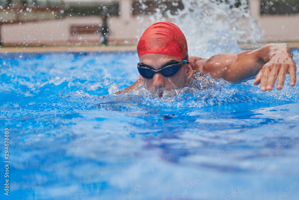 Swimmer in an outdoor pool, swimming in the crawl style, pulling his head out of the water, with his arms back, seen from the front at the water level