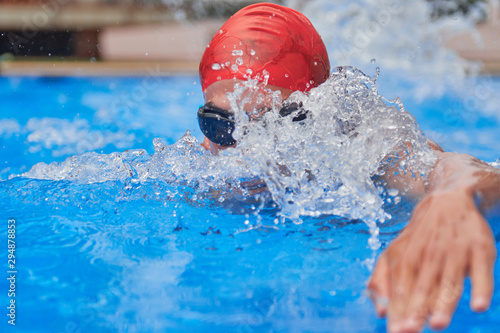 Swimmer in an outdoor pool, swimming in the crawl style, taking the head out of the water, has the texture of the water on the face, seen from the water level front © Albert