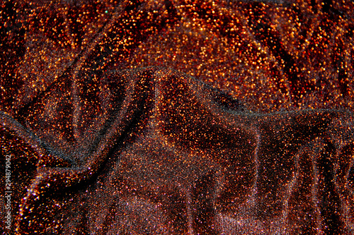 A shiny wavy surface of a brown fabric with orange lurex threads as a background photo