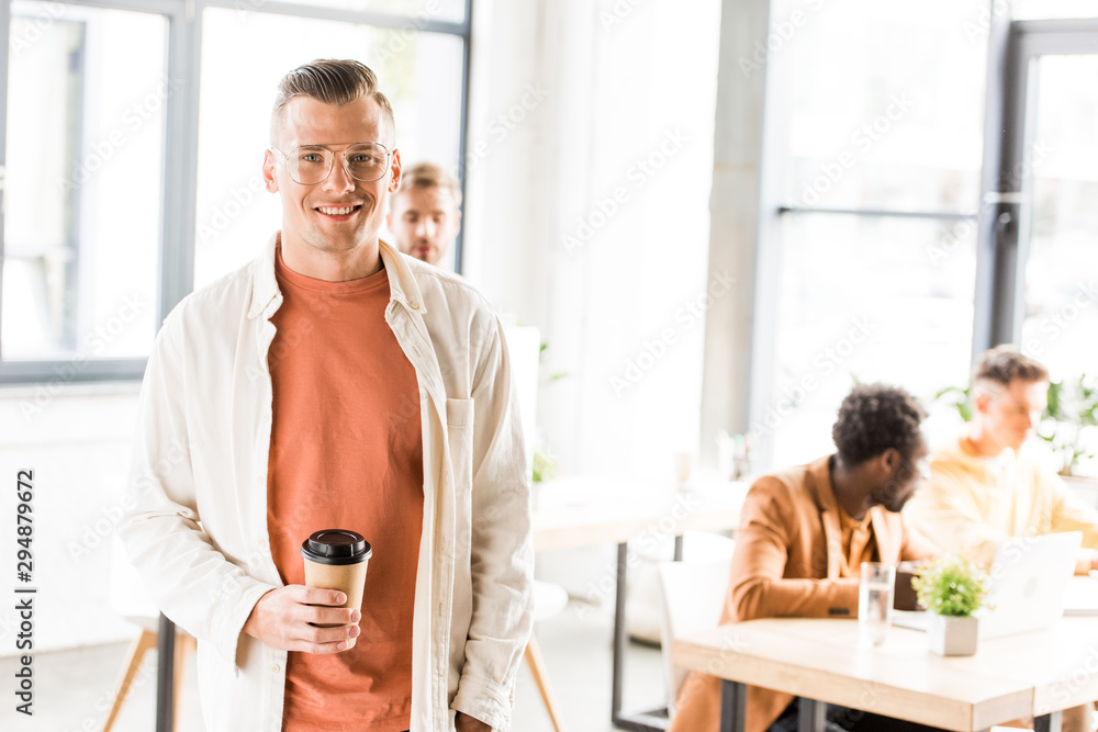 young, handsome businessman holding coffee to go and smiling at camera young, handsome businessman holding coffee to go and smiling at camera