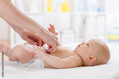 Photographie Woman putting diaper on baby on bed in nursery room