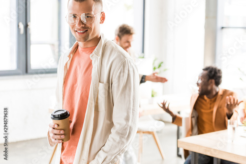 young, handsome businessman holding coffee to go and smiling at camera