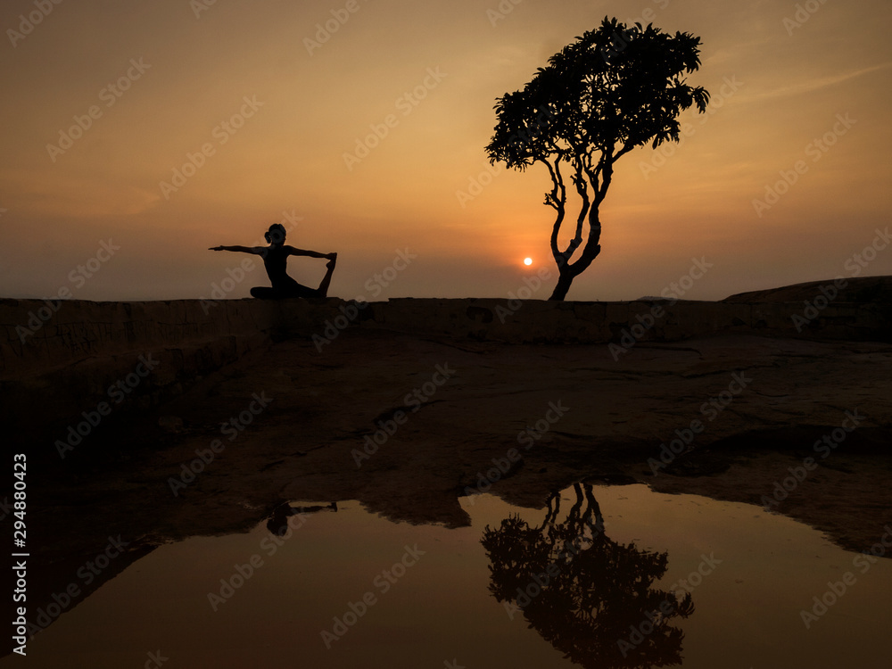 Girl doing yoga stretch at sunset, Anjanadri Hill, Hampi, Karnataka, India	