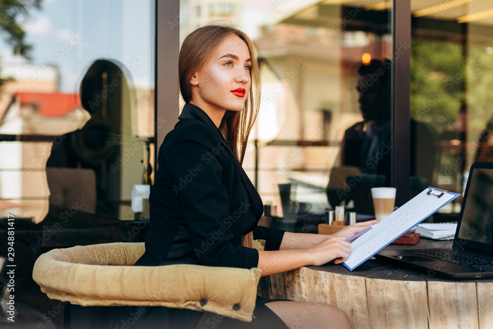 Portrait of blond businesswoman in cafe  holding a document and looking up dreamly outdoor