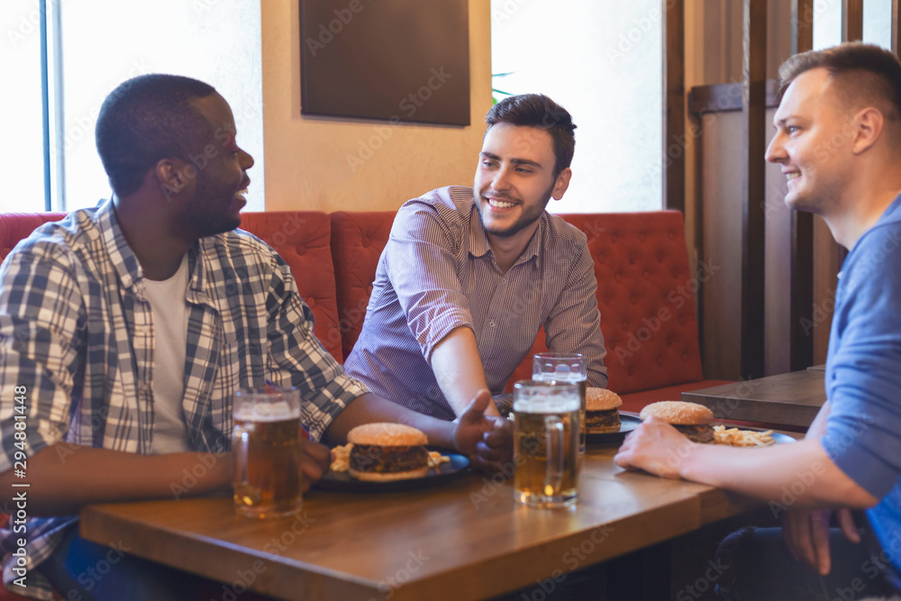 Three young men eating burgers and drinking beer Three young men eating burgers and drinking beer