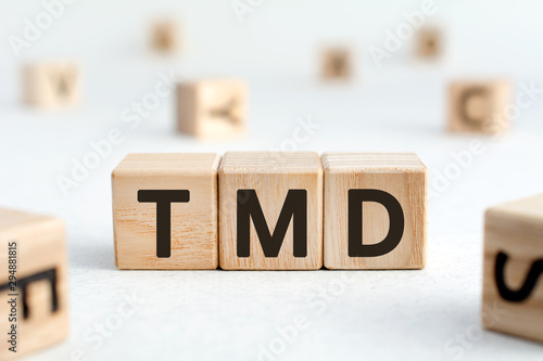 TMD - acronym from wooden blocks with letters, abbreviation TMJ temporomandibular joint syndrome, TMD Temporomandibular disorder concept, random letters around, white  background photo