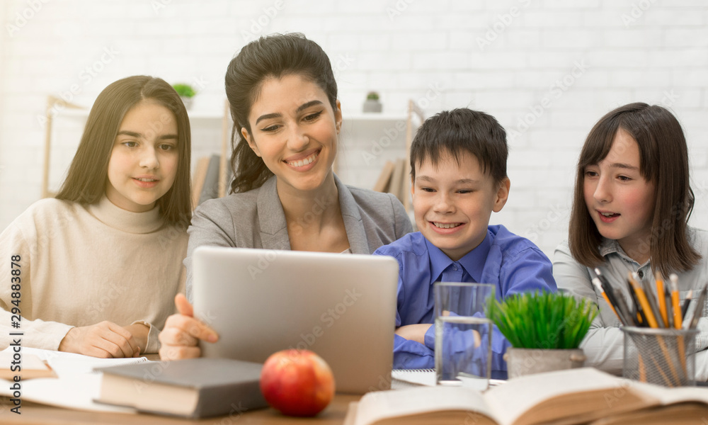 Children and female teacher looking on tablet at lesson