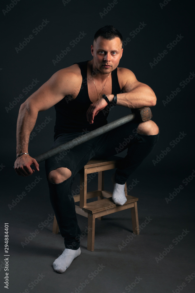 Obraz premium young bodybuilder in black clothes with a sledgehammer in his hands. Studio photography