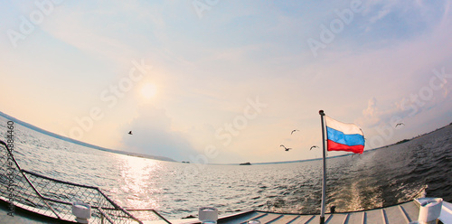 The Russian flag flies in the wind, against the background of water and blue cloudy sky.