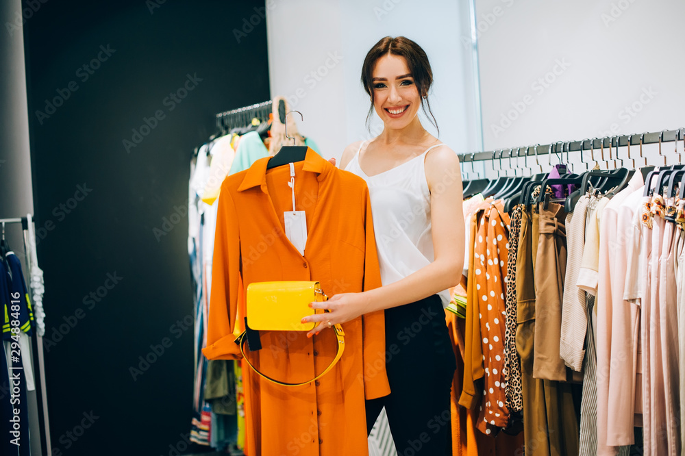 Perfect combinations of dress and bag! Beautiful young woman trying to  choose clothes to herself or customer while working in the fashion  boutique. Fashion stylist show new collection and in store Stock
