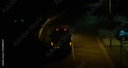  A British Ambulance Driving Down a Dark Road Leaving For An Emergency Late at Night. Driving to an Incident. Dark Dim Empty Road With Very Little Street Lights Leading To A Main Road.