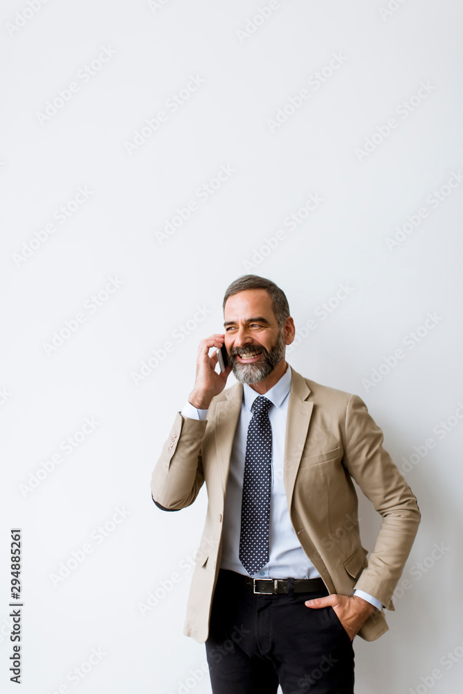 Senior businessman using mobile phone against wall in office Senior businessman using mobile phone against wall in office