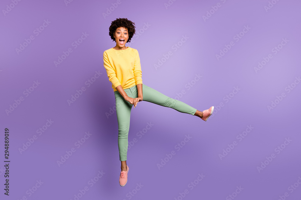 Full size photo of cheerful funny funky teen afro american girl jump have fun on autumn weekends spring free time wear yellow pullover green pants trousers isolated over purple violet color background