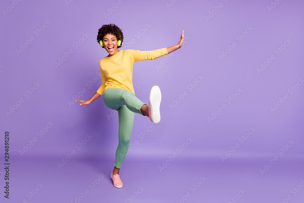 Full length body size photo of wavy cheerful excited ecstatic overjoyed shouting girlfriend dancing listening to music pretending to be kicking with leg near empty space isolated over violet color