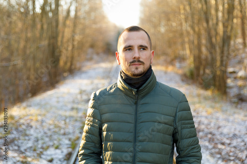 Young man wearing green puffer jacket on snowy road through forest
