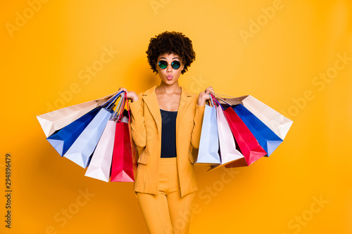 Portrait of funny funky brunette wavy hair afro american lady on leisure travel hold bags shopping purchase addicted person wear style sunglass outfit pants trousers isolated yellow color background photo