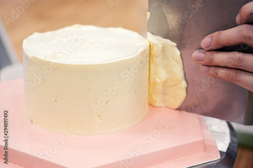 Woman frosting a cake with buttercream on a rotating turntable with a stainless steel dough scraper.