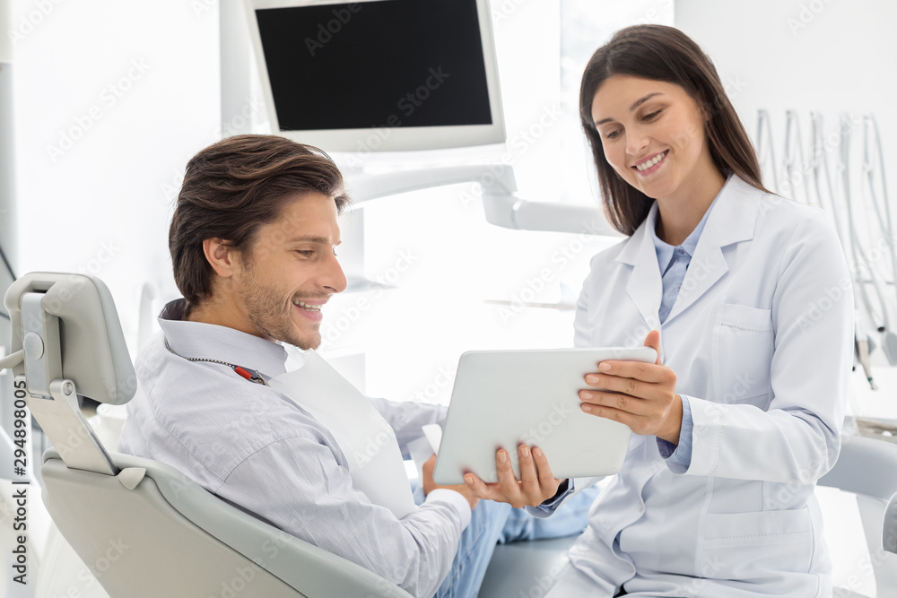 Cheerful dentist showing patient results of treatment on digital tablet Cheerful dentist showing patient results of treatment on digital tablet
