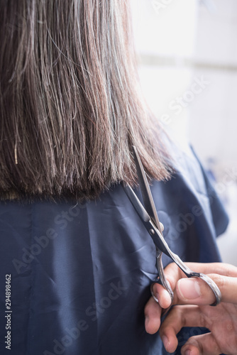 Close-up of hand and scissors trimming a young asian woman's hair.