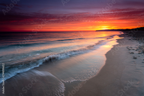 Sunrise at sandy beach in Baabe  slow incoming waves  morning sky with orange sunrise  Ruegen island  Baltic Sea  Germany.