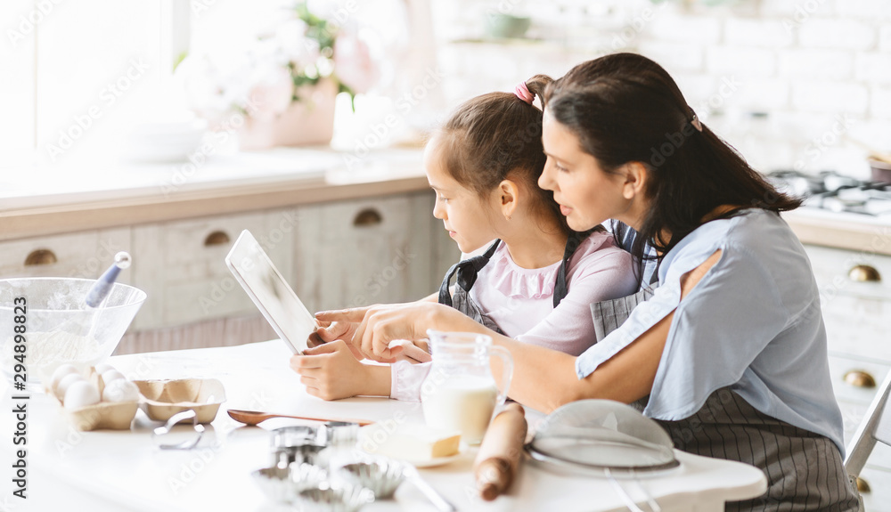 Little girl and her mother using digital tablet in kitchen Little girl and her mother using digital tablet in kitchen