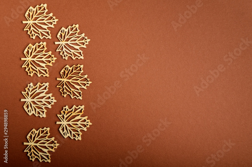 Seven delicate light brown wooden leaves on textured brown cardboard background, displayed on left side, top view with space for text on the right side, flat lay with laser cut wooden objects, selecti photo