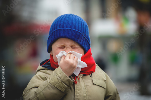 School child boy blow his nose. Sick child with napkin in autumn park. Allergic kid, flu season. Kid with cold rhinitis, get cold. Back to school