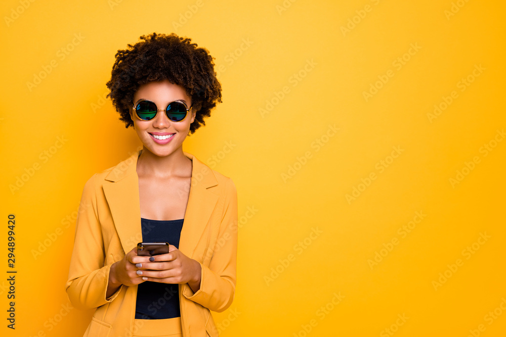 Portrait of positive cheerful afro american girl in sunglass use her smartphone type text post comments feedback read feednews wear stylish trendy suit clothes isolated over yellow collor background Portrait of positive cheerful afro american girl in sunglass use her smartphone type text post comments feedback read feednews wear stylish trendy suit clothes isolated over yellow collor background